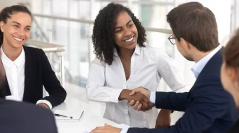 3 pessoas em um escritorio aonde tem 1 homem e uma mulher apertando a mao e sorrindo