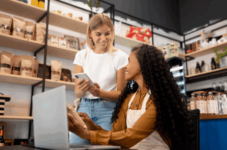 olaboradoras em um ambiente de varejo corporativo analisando informações no laptop e no celular, discutindo melhorias no desempenho da loja.